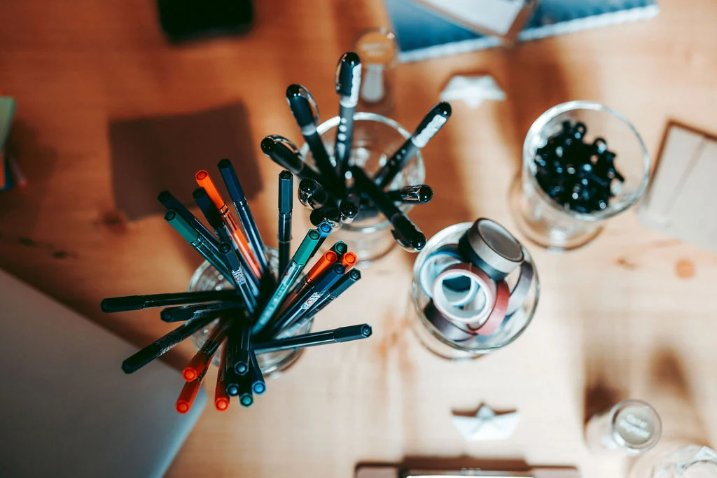 Top-down view of pens and workshop material on a wooden table